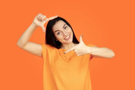 Caucasian young womans portrait on orange studio background. Beautiful female brunette model in shirt. Concept of human emotions, facial expression, sales, ad. Copyspace. Posing and smiling.の写真素材