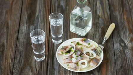 Vodka with salted herring and onion on wooden background. Alcohol pure craft drink and traditional...