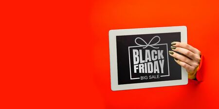 Hands holding tablet screen with black friday lettering on red background. Concept of sales, black friday, cyber monday, finance, business, money. Online shops and payments bill.の写真素材