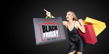 Young blonde woman in dress shopping on black background. Attractive caucasian female model. Finance, black friday, cyber monday, sales, autumn concept. Copyspace. Smiling, screaming happy.の写真素材