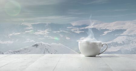 Single tea or coffee cup and landscape of mountains on background. Cup of hot drink with snowly look and cloudly sky in front of it. Warm in winter day, holidays, travel, New Year and Christmas time.の写真素材