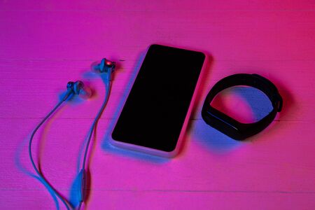Top view of set of gadgets in purple neon light and pink background. Smartphone and smartwatch, headphones. Copyspace for your advertising. Tech, modern, gadgets.の写真素材