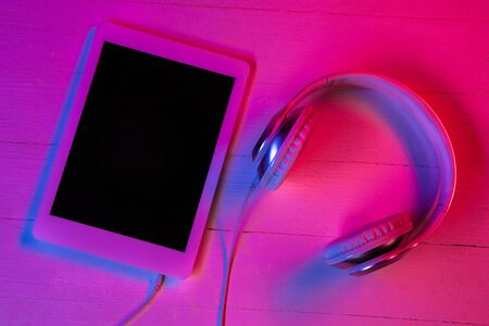 Top view of set of gadgets in purple neon light and pink background. Tablet with black screen and...