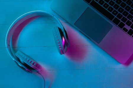 Top view of set of gadgets in purple neon light and blue background. Laptop and headphones on wooden table. Copyspace for your advertising. Tech, modern, gadgets.の写真素材