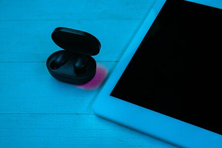 Top view of set of gadgets in purple neon light and blue background. Tablet and wireless headphones...