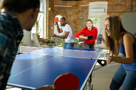 Young people playing table tennis in workplace, having fun. Friends in casual clothes playng together at sunny day. Concept of leisure activity, sport, friendship, teambuilding, teamwork.の写真素材
