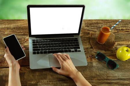 Blank screens of laptop and smartphone on a wooden table outdoors with nature on background, mock up. Fruits and fresh juice near by. Concept of creative workplace, business, freelance. Copyspace.の写真素材