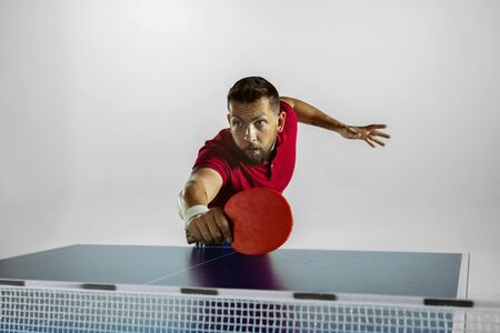 Strong. Young man plays table tennis on white studio background. Model plays   table tennis. Concept of leisure activity, sport, human emotions in gameplay, healthy lifestyle, motion, action, movement.の写真素材