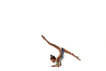 Little flexible girl isolated on white studio background. Little female model as a rhythmic gymnastics artist in bright leotard. Grace in motion, action and sport. Doing exercises with the ball.の写真素材
