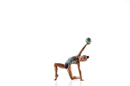 Little flexible girl isolated on white studio background. Little female model as a rhythmic gymnastics artist in bright leotard. Grace in motion, action and sport. Doing exercises with the ball.の写真素材