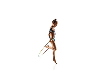 Little flexible girl isolated on white studio background. Little female model as a rhythmic gymnastics artist in bright leotard. Grace in motion, action and sport. Doing exercises with the hoop.の写真素材