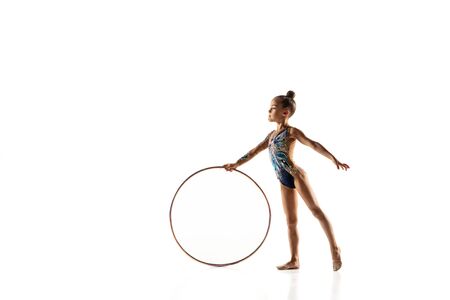 Little flexible girl isolated on white studio background. Little female model as a rhythmic gymnastics artist in bright leotard. Grace in motion, action and sport. Doing exercises with the hoop.の写真素材