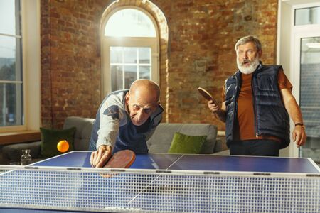 Senior men playing table tennis in workplace, having fun. Friends in casual clothes play table tennis together at sunny day. Concept of leisure activity, sport, friendship, teambuilding, teamwork.の写真素材