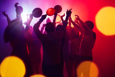 Together. A crowd of people in silhouette raises their hands on dancefloor on neon light background. Night life, club, music, dance, motion, youth. Purple-pink colors and moving girls and boys.の写真素材