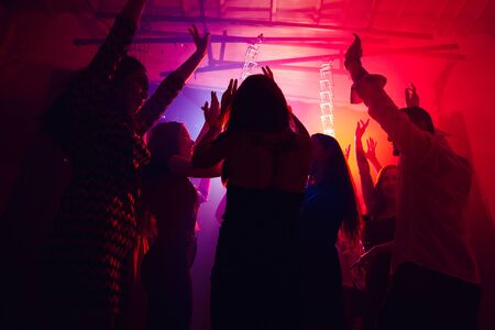Until the morning. A crowd of people in silhouette raises their hands on dancefloor on neon light background. Night life, club, music, dance, motion, youth. Purple-pink colors and moving girls and boys.の写真素材