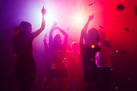 Rhythm. A crowd of people in silhouette raises their hands on dancefloor on neon light background. Night life, club, music, dance, motion, youth. Purple-pink colors and moving girls and boys.の写真素材