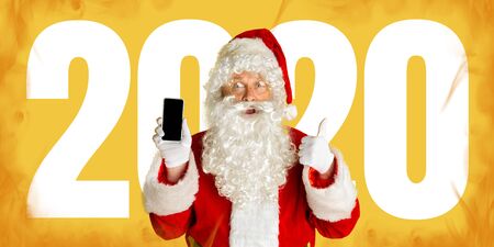 Santa Claus in sunglasses isolated on yellow studio background. Caucasian male model in traditional...