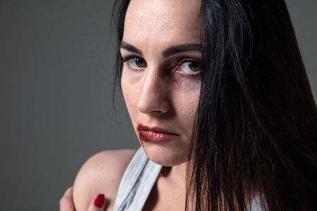 Woman in fear of domestic abuse and violence, concept of female rights. Caucasian brunette woman on grey background looks upset, sad, depressed being victim of man or husband. Has bruises, hematomas.の写真素材