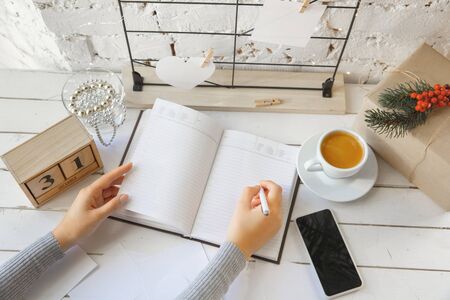 Writes wishes. Dreams of goals plans make a list for writing in notebook. Female hands on a background with wooden calendar, giftbox for New Year, winter holidays and Christmas time. Preparing moodboard.の写真素材