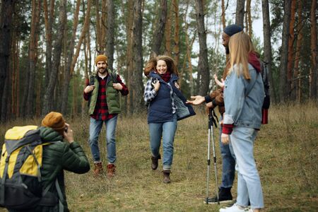 Group of friends on a camping or hiking trip in autumn day. Men and women with touristic backpacks going throught the forest, talking, laughting. Leisure activity, friendship, weekend.の写真素材