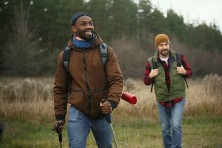 Group of friends on a camping or hiking trip in autumn day. Men and women with touristic backpacks going through the forest, talking, laughing. Leisure activity, friendship, weekend.の写真素材