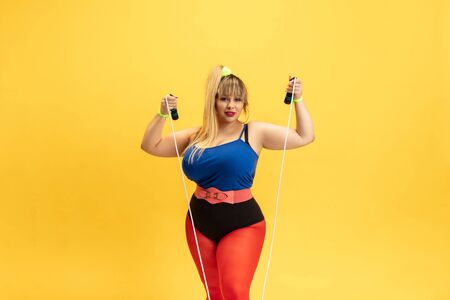 Young caucasian plus size female models training on yellow background. Stylish woman in bright...