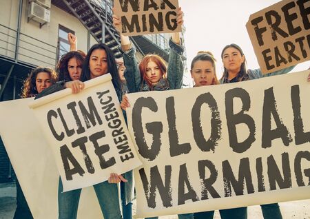Young woman with poster in front of people protesting about climate changing on the street. Meeting about problem in ecology, environment, global warming, industrial influence, climate emergency.の写真素材