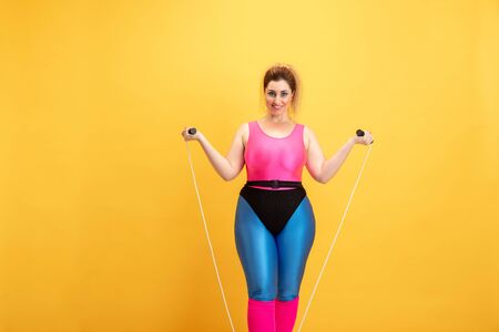 Young caucasian plus size female models training on yellow background. Copyspace. Concept of sport, healthy lifestyle, body positive, fashion, style. Stylish woman practicing with jump rope and smiling.の写真素材