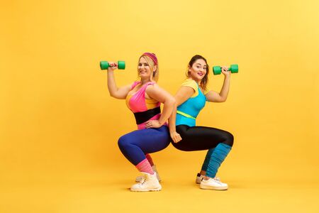 Young caucasian plus size female models training on yellow background. Copyspace. Concept of sport, healthy lifestyle, body positive, fashion. Friendship, girl power. Stylish woman practicing, smiling.の写真素材