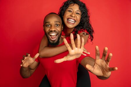 Young emotional african-american man and woman in bright casual clothes posing on red background. Concept of human emotions, facial expession, relations, ad. Cute couple hugging and laughting.の写真素材
