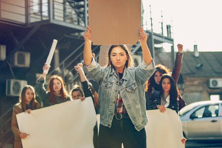 Young woman with blank poster in front of people protesting about womens rights and equality on the...