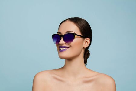 Portrait of beautiful woman with bright make-up and sunglasses on blue studio background. Stylish, fashionable make and hairstyle. Colors of summer. Beauty, fashion and ad concept. Smiling.の写真素材