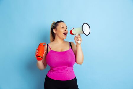 Young caucasian plus size female models training on blue background. Concept of sport, human emotions, expression, healthy lifestyle, body positive, equality. Posing with bottle and mouthpeace.の写真素材