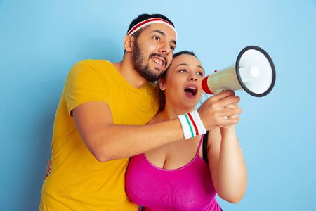 Young pretty caucasian couple in bright clothes training on blue background Concept of sport, human emotions, expression, healthy lifestyle, relation, family. Sales. Calling together in mouthpeace.の写真素材