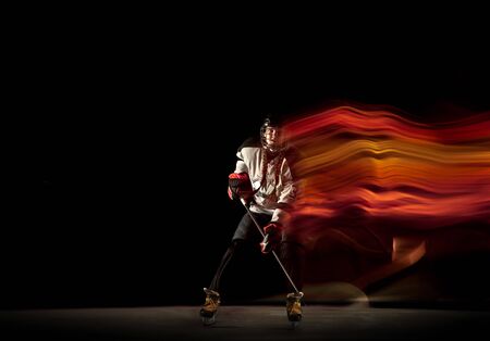 Young female hockey player with the stick on black background and neon light. Sportswoman wearing...