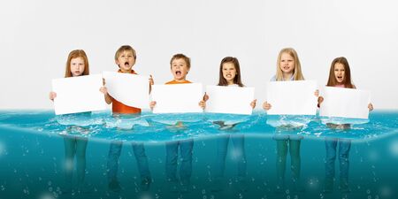 Drowned at home. Group of children with blank banners standing in water of melting glacier, global warming. Ecology, environmental concept. Save planet for future generation, stop overusing nature.の写真素材