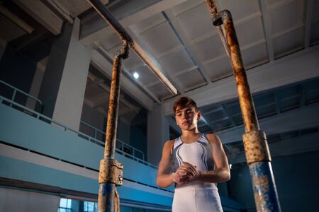 Little male gymnast training in gym, flexible and active. Caucasian fit little boy, athlete in white sportswear preparing for exercises for strength, balance. Movement, action, motion, dynamic concept.の写真素材