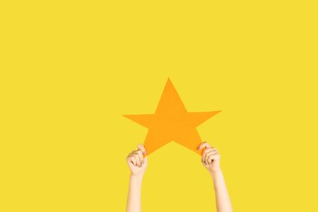 Hands holding the sign of star on yellow studio background. Negative space to insert your text or image, advertising. Social media, showing meaning, communication, gadgets, modern technologies.の写真素材