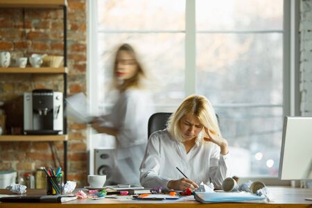 Nervous and tired boss at her workplace busy while people moving near blurred. Office worker,...