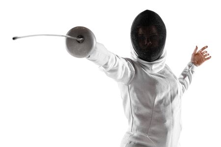 Teen girl in fencing costume with sword in hand isolated on white studio background. Young female caucasian model practicing and training in motion, action. Copyspace. Sport, youth, healthy lifestyle.の写真素材