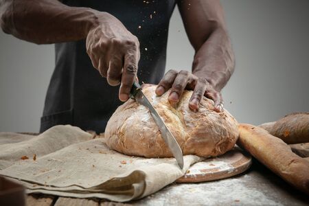 Close up of african-american man slices fresh cereal, white bread, bran with a kitchen knife on...