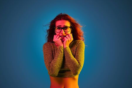Caucasian womans portrait isolated on blue studio background in neon light. Beautiful female model...