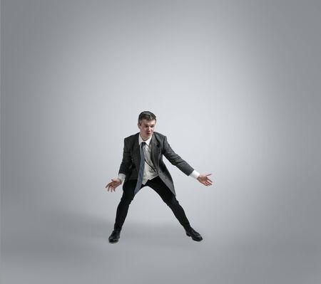 Dreams about big possibilities. Man in office clothes traines in football or soccer like goalkeeper on grey background. Unusual look for businessman in motion, action. Sport, healthy lifestyle.の写真素材