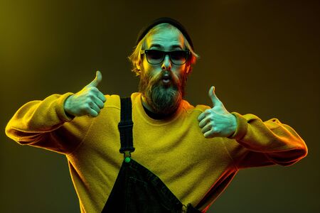Caucasian womans portrait on gradient studio background in neon light. Beautiful male model with hipster style in glasses. Concept of human emotions, facial expression, sales, ad. Thumbs up.の写真素材