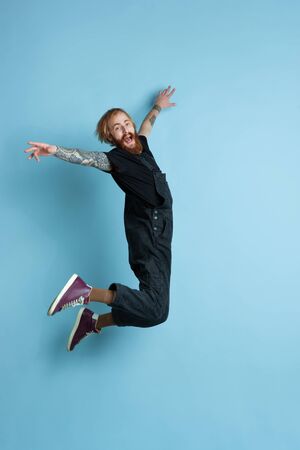 Portrait of young caucasian man looks dreamful, cute and happy. Jumping. laughting on blue studio background. Copyspace for your advertising. Concept of future, target, dreams, visualisation.の写真素材