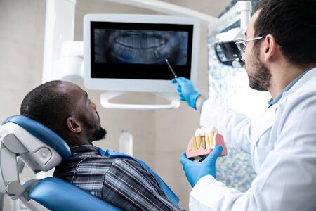 Young african-american man visiting dentist's office for prevention and treatment of the oral cavity. Man and male doctor while checkup teeth. Healthy lifestyle, healthcare and medicine concept.の写真素材