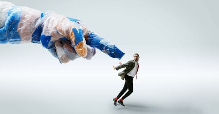 Young caucasian man avoiding big plastic hand on white studioの写真素材