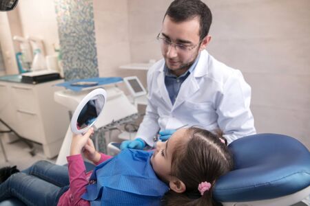 Young caucasian girl calm and happy visiting dentists office for prevention and treatment of the oral cavity. Child and doctor while checkup teeth. Healthy lifestyle, healthcare and medicine concept.の写真素材