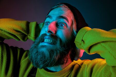 Exremely shocked, astonished. Caucasian mans portrait on gradient studio background in neon light. Beautiful male model with hipster style. Concept of human emotions, facial expression, sales, ad.の写真素材