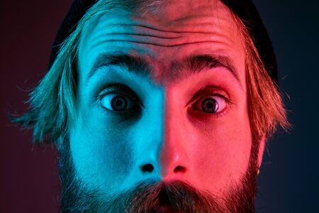 Shocked, astonished, close up. Caucasian mans portrait on gradient studio background in neon light. Beautiful male model with hipster style. Concept of human emotions, facial expression, sales, ad.の写真素材